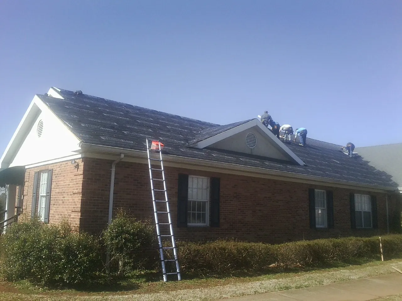Crew tearing shingles off a brick ranch roof with a ladder set — Metal Roof Repair work by our crew in Canal Winchester