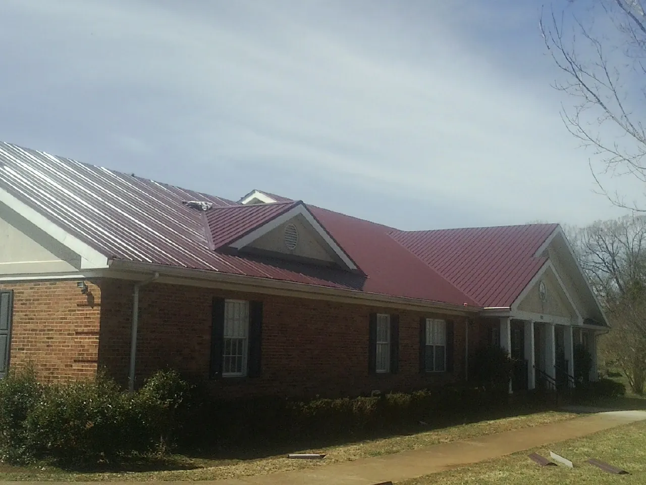 Red metal roof with gabled entries on a long brick building, from a Hail Damage Roof Repair job in Canal Winchester