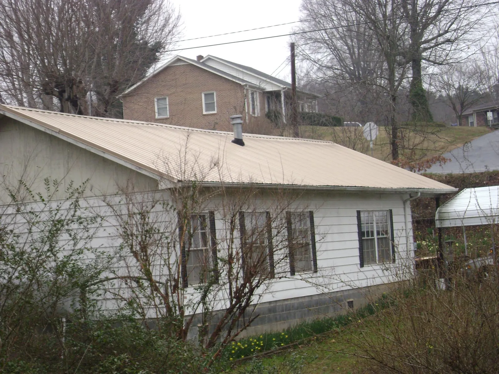 Tan metal roof on a white sided house set into a hillside — Commercial Roofing by Roofing Brothers in Canal Winchester